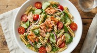 Fresh fusilli pasta salad with grilled chicken, cherry tomatoes, mozzarella and basil leaves in white bowl on rustic wooden table for healthy meal preparation.