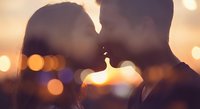 Romantic couple silhouettes touching foreheads intimately against warm bokeh lights background at sunset creating dreamy atmosphere for love concepts.