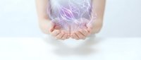 Female hands cupped together holding glowing purple energy light with flowing ethereal wisps against white background for healing and spiritual concepts.