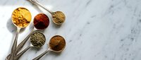 Colorful aromatic spices in metal measuring spoons on white marble surface for cooking and seasoning recipes.
