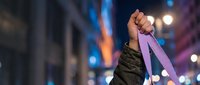 Young adult male with medium skin tone holding purple ribbon overhead in urban nighttime setting, symbolizing awareness and support for causes.