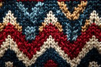 Close-up of knitted zigzag pattern in red, white, navy blue and light blue wool yarn showing detailed texture and traditional chevron design for winter fashion.