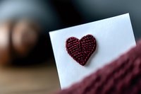 Burgundy knitted heart decoration on white paper card with soft blur background, romantic handmade Valentine greeting concept for love messages.