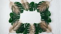 Tropical frame with golden palm leaves and green monstera foliage surrounding blank white space for text or design on neutral background.