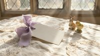 Elegant wedding invitation with purple ribbon on vintage lace tablecloth near window with natural sunlight creating romantic atmosphere for ceremony planning.