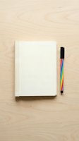 Blank notebook with rainbow marker on light wooden surface, flat lay composition for creative writing, planning, and design projects.