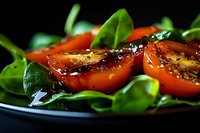 Fresh spinach salad with grilled tomato slices seasoned with herbs and pepper on dark plate. Healthy vegetarian meal ready for restaurant serving.