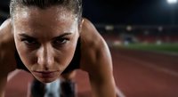 Determined female athlete in starting position on running track at night stadium ready to sprint with intense focused expression for sports competition.