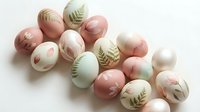 Pastel Easter eggs with botanical leaf patterns in pink green and cream colors arranged on white background for spring holiday decoration.