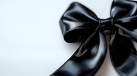 Elegant black satin bow against white background, close-up view showing luxurious sheen and texture. Suitable for gift wrapping, fashion, and luxury product designs.