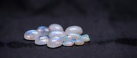 Collection of translucent moonstone gemstones with iridescent blue flash arranged on dark textured surface for jewelry making and mineral specimens.