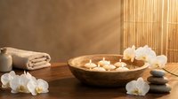 Spa wellness setup with floating candles in wooden bowl, white orchids, massage stones and towels creating peaceful relaxation atmosphere for meditation.