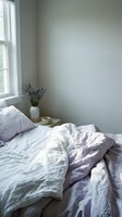 Serene bedroom corner with unmade bed featuring lavender and white linens, potted dried flowers, and natural light from window for home decor.