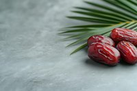 Fresh dates with palm leaf on gray stone surface for healthy snacking and Middle Eastern cuisine preparation.