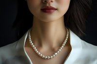 Close up portrait of young Asian woman wearing elegant pearl necklace and white blouse against dark background, focus on neck and lips area.