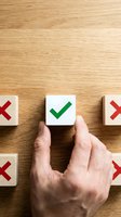 Hand picking wooden block with green checkmark among blocks with red crosses on wooden surface, symbolizing right choice.