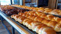 Fresh baked sweet bread rolls displayed in rows on wooden counter at bakery, showing golden brown crusts and soft texture, ready for retail sale.