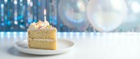 Slice of vanilla birthday cake with lit candle on white plate against sparkling blue bokeh lights background for celebration and party occasions.