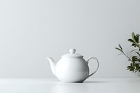 Classic white ceramic teapot on minimal light background with green plant leaves. Clean composition for food and beverage marketing.