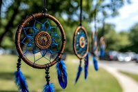 Native American dreamcatcher with blue feathers and intricate woven pattern hanging outdoors in natural sunlight, selective focus on front ornament with blurred background.