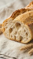 Freshly baked artisan bread slice with airy texture and golden crust on linen cloth with wheat stalks for bakery and food photography.