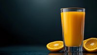 Fresh orange juice in tall glass with cut oranges on dark background, dramatic lighting creates appetizing beverage presentation for menu or advertising.