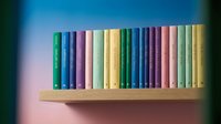 Colorful hardcover books arranged on wooden shelf against gradient background, suitable for library, education, and interior design projects.