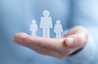 Hand holding white paper family figures against soft blue background, representing family protection, social services, and parental care concept.
