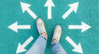 Person in sneakers standing at center of white directional arrows on turquoise ground, symbolizing choices, decisions, career paths and life direction options.