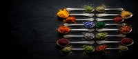 Colorful spices and herbs arranged in metal spoons on dark wooden background for culinary cooking and seasoning recipes.