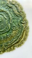 Macro close-up of weathered green patina surface with ornate carved relief details and textured layers, suitable for backgrounds and design elements.