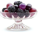 Fresh blackberries and red grapes arranged in elegant glass dessert bowl on white background, macro food photography highlighting natural textures and colors.