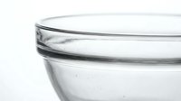 Transparent glass bowl closeup on white background, showing clear texture and rim detail for kitchen, cooking, and food styling concepts.