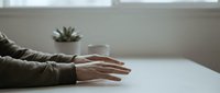 Relaxed hands resting on white table surface in bright minimalist interior with succulent plant creating peaceful workspace atmosphere for meditation wellness.