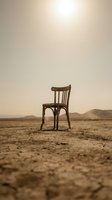 Wooden chair sitting alone on barren desert landscape with cracked earth and distant mountains under hazy sky, conveying isolation, abandonment, and desolation for conceptual and editorial use.