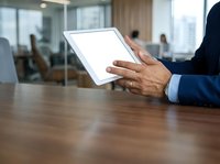Businessman with dark skin tone holding blank tablet device at wooden desk in modern office with city skyline view, suitable for corporate technology and business applications.