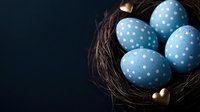 Spotted blue Easter eggs in dark nest with decorative golden heart, dramatic lighting on black background creates elegant holiday composition.