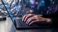 Hands of a young Caucasian male professional typing on a laptop with glowing digital particles in a dark tech environment.