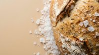 Artisan sourdough bread loaf with coarse sea salt crystals on rustic beige background. Fresh baked crusty bread for bakery, cooking and food photography.