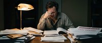 Stressed middle-aged businessman working late at office desk with papers and documents under warm lamp light in dark room for overtime concept.