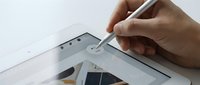 Hand holding stylus pen drawing on white digital tablet screen for creative design work and digital art projects.