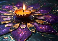 Lit candle in ornate golden flower-shaped holder with purple and gold glitter petals on dark surface, creating festive ambiance for celebrations, meditation, or spiritual rituals.
