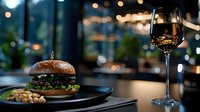 Gourmet beef burger on black plate with glass of red wine in luxurious restaurant setting. Blurred bokeh lights create elegant atmosphere. Food photography for menus.
