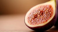 Fresh ripe fig cut in half showing juicy pink flesh and seeds with soft natural lighting on blurred background, macro food photography.