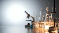 Laboratory glassware and microscope on white table with warm lighting for scientific research and medical testing applications.