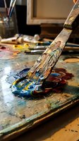 Artist paintbrush covered in colorful acrylic paint on messy palette in creative studio workspace for artistic projects and creative expression.
