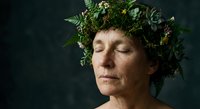 Serene mature Caucasian woman with eyes closed wearing natural green foliage crown against dark background for wellness and nature connection concepts.
