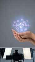 Female hands holding glowing medical icons including heartbeat, cross symbols, and hearts on gray background. Healthcare, wellness, and telemedicine concept for medical services and insurance.
