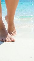 Woman bare feet walking on white sandy beach with turquoise ocean water in background. Summer vacation and tropical travel concept.
