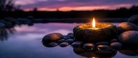 Zen candle burning on stone arrangement by tranquil lake at sunset creating peaceful meditation atmosphere with purple sky reflection in calm water.